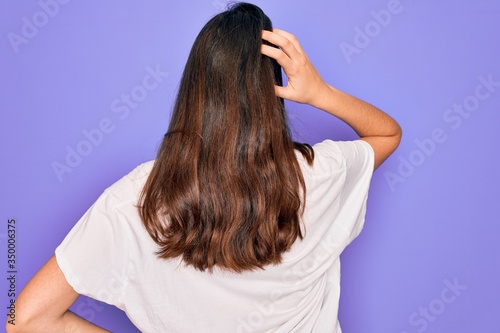 Young beautiful brunette woman wearing casual white t-shirt over purple background Backwards thinking about doubt with hand on head