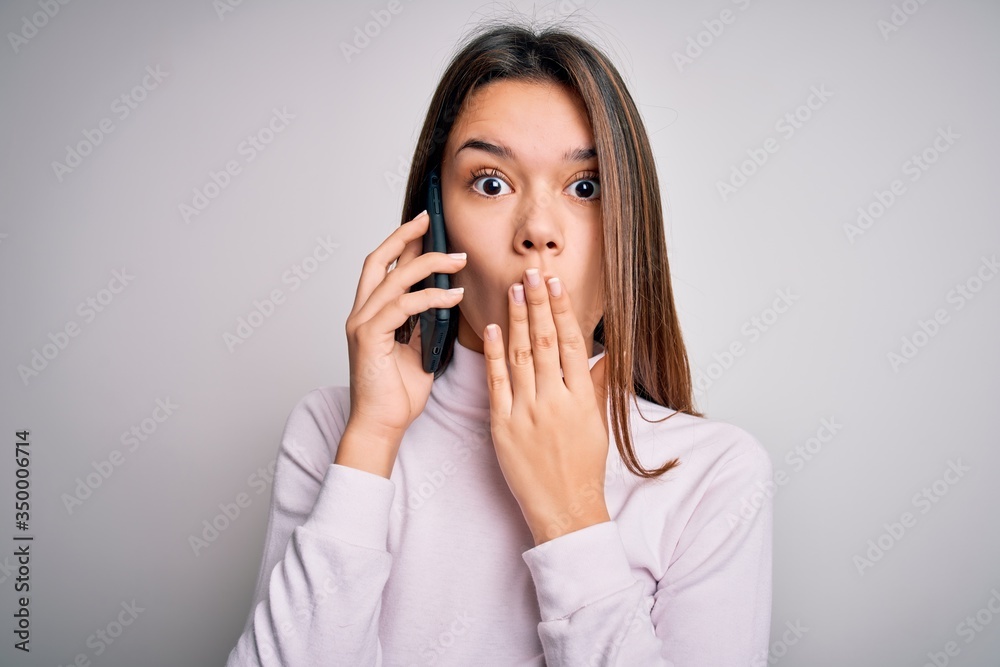 Beautiful brunette girl having conversation talking on the smartphone over white background cover mouth with hand shocked with shame for mistake, expression of fear, scared in silence, secret concept Beautiful brunette girl having conversation talking on the smartphone over white background cover mouth with hand shocked with shame for mistake, expression of fear, scared in silence, secret concept