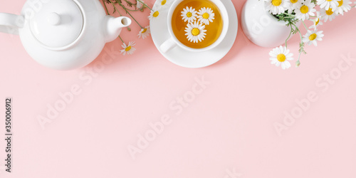 White chamomiles, cup and teapot on pastel pink background. Herbal tea of chamomile flower. Chamomile tea concept. Flat lay, top view, copy space