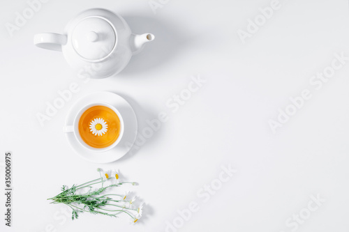 White chamomiles and teapot on white background. Herbal tea of chamomile flower. Chamomile tea concept. Flat lay, top view, copy space