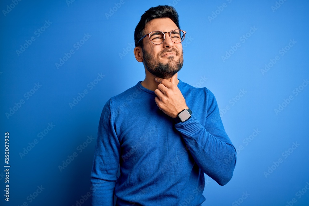 Young handsome man with beard wearing casual sweater and glasses over blue background Touching painful neck, sore throat for flu, clod and infection