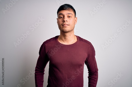 Young handsome hispanic man wearing casual shirt standing over white isolated background Relaxed with serious expression on face. Simple and natural looking at the camera.