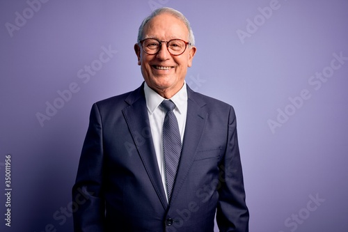 Obraz na płótnie Grey haired senior business man wearing glasses and elegant suit and tie over purple background with a happy and cool smile on face