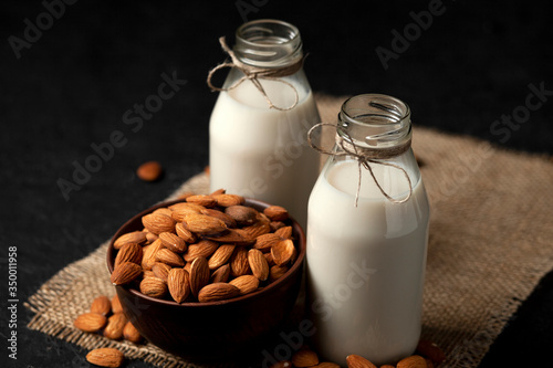 two bottles of almond milk with nuts on a dark black table, vegetarian milk without sugar and lactose