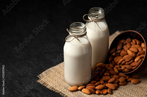 almond milk in bottles with nuts on a black table, a variety of dairy products without sugar and lactose, a vegetarian drink