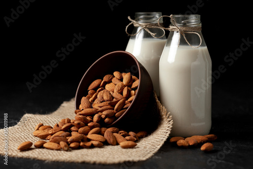 lactose-free almond milk in bottles with nuts on a black table, vegetarian milk drink, healthy milk product