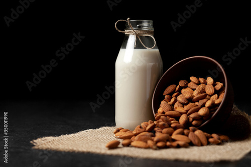 almond milk in bottle with nuts on a dark black table, a variety of dairy products without sugar and lactose