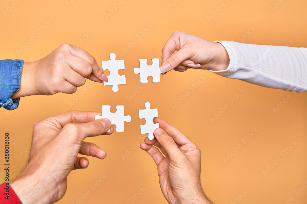 Hands of caucasian young people connecting pieces of puzzle over isolated yellow background Hands of caucasian young people connecting pieces of puzzle over isolated yellow background