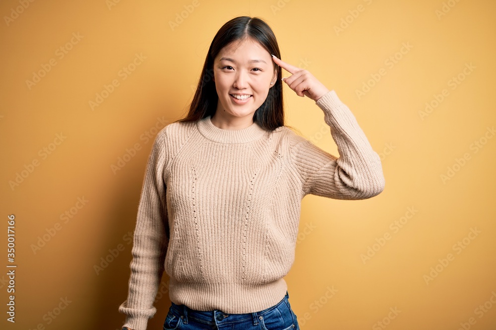 Young beautiful asian woman wearing casual sweater over yellow isolated background Smiling pointing to head with one finger, great idea or thought, good memory