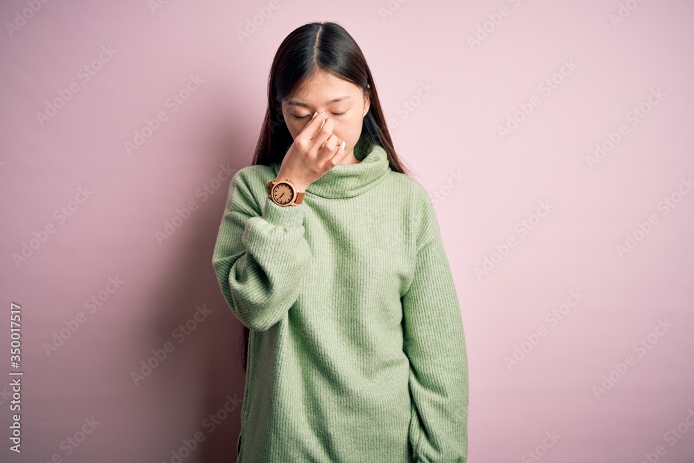 Young beautiful asian woman wearing green winter sweater over pink solated background tired rubbing nose and eyes feeling fatigue and headache. Stress and frustration concept. Young beautiful asian woman wearing green winter sweater over pink solated background tired rubbing nose and eyes feeling fatigue and headache. Stress and frustration concept.