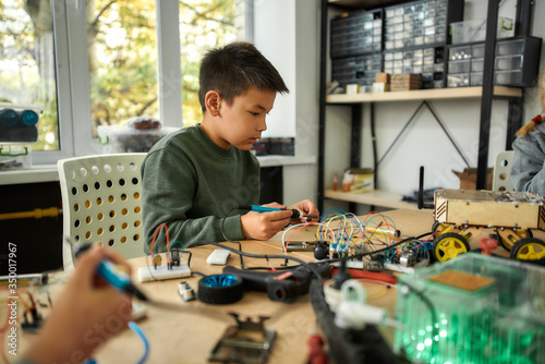 Passion that builds excellence. Young engineer using soldering iron to join chips and wires. Robotics and software engineering for elementary students. Inventions and creativity for kids