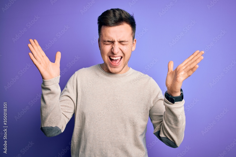 Young handsome caucasian man wearing casual sweater over purple isolated background celebrating mad and crazy for success with arms raised and closed eyes screaming excited. Winner concept Young handsome caucasian man wearing casual sweater over purple isolated background celebrating mad and crazy for success with arms raised and closed eyes screaming excited. Winner concept