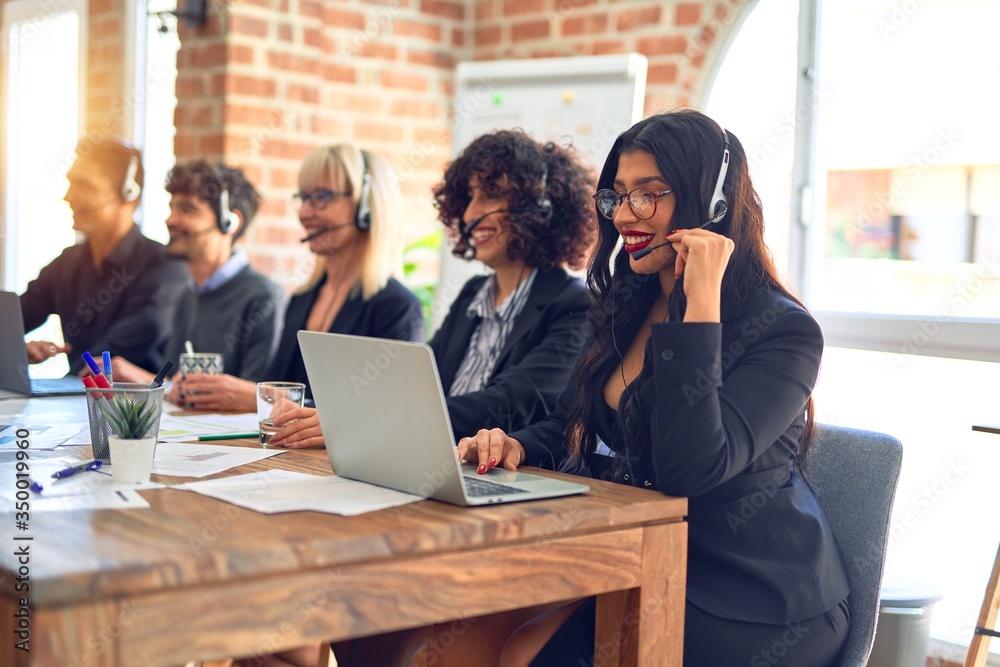 Fototapeta premium Group of call center workers smiling happy and confident. Working together with smile on face using headset at the office.