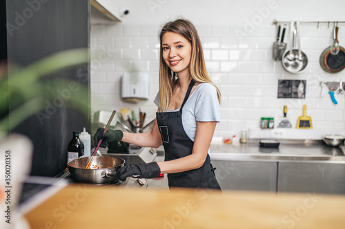 Beautiful happy young woman preparing pasta with tomato sous for dinner.