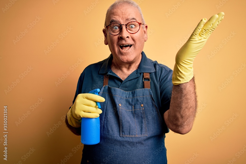 Middle age hoary cleaner man cleaning wearing apron and gloves using sprayer very happy and excited, winner expression celebrating victory screaming with big smile and raised hands Middle age hoary cleaner man cleaning wearing apron and gloves using sprayer very happy and excited, winner expression celebrating victory screaming with big smile and raised hands