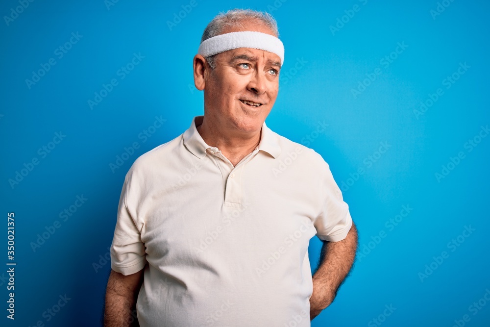 Middle age hoary sportsman doing sport wearing sportswear over isolated blue background looking away to side with smile on face, natural expression. Laughing confident.