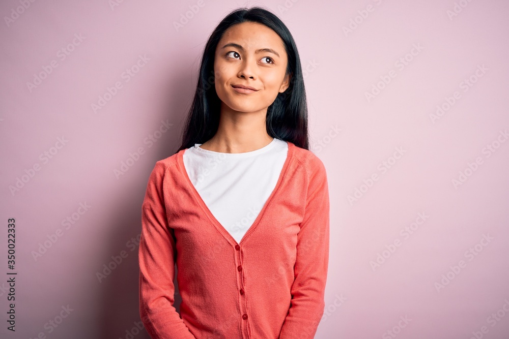 Fototapeta premium Young beautiful chinese woman wearing casual sweater over isolated pink background smiling looking to the side and staring away thinking.
