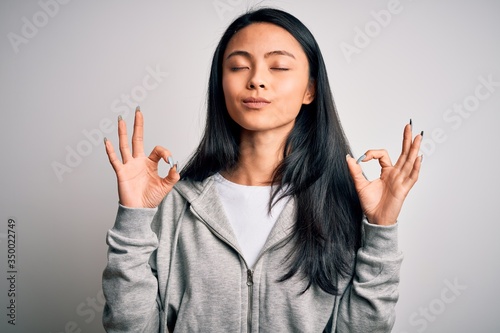 Young beautiful chinese sporty woman wearing sweatshirt over isolated white background relax and smiling with eyes closed doing meditation gesture with fingers. Yoga concept.