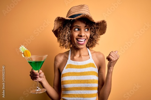 African american tourist woman with curly on vacation wearing summer hat drinking cocktail pointing and showing with thumb up to the side with happy face smiling