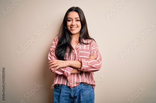 Young brunette woman wearing casual striped shirt over isolated background happy face smiling with crossed arms looking at the camera. Positive person.