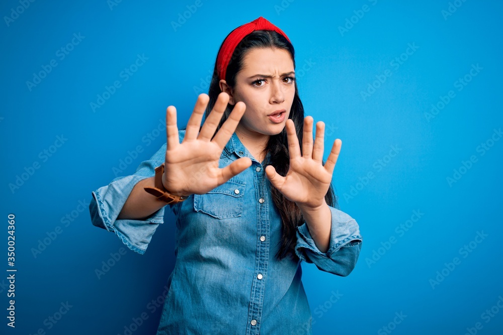 Young brunette woman wearing casual denim shirt over blue isolated background doing stop gesture with hands palms, angry and frustration expression Young brunette woman wearing casual denim shirt over blue isolated background doing stop gesture with hands palms, angry and frustration expression