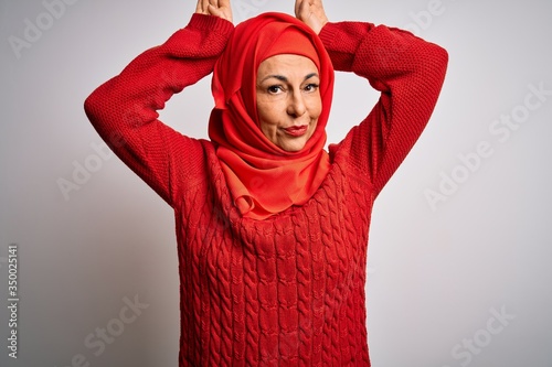 Middle age brunette woman wearing muslim traditional hijab over isolated white background Doing bunny ears gesture with hands palms looking cynical and skeptical. Easter rabbit concept. © Krakenimages.com