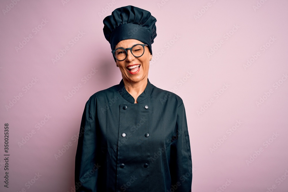 Middle age brunette chef woman wearing cooker uniform and hat over isolated pink background winking looking at the camera with sexy expression, cheerful and happy face. Middle age brunette chef woman wearing cooker uniform and hat over isolated pink background winking looking at the camera with sexy expression, cheerful and happy face.