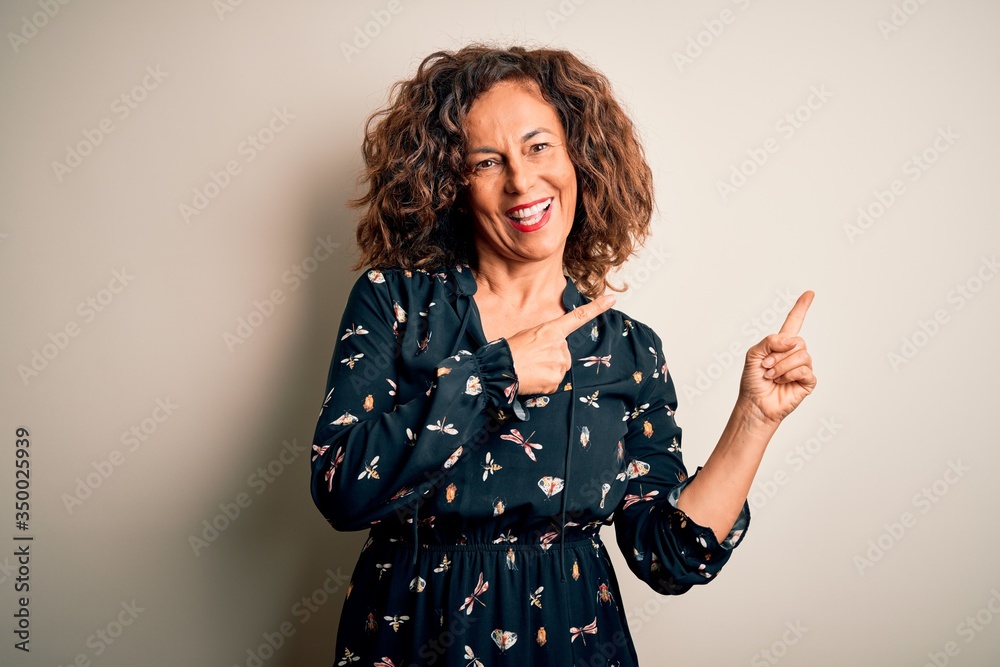 Middle age beautiful woman wearing casual dress standing over isolated white background smiling and looking at the camera pointing with two hands and fingers to the side. Middle age beautiful woman wearing casual dress standing over isolated white background smiling and looking at the camera pointing with two hands and fingers to the side.