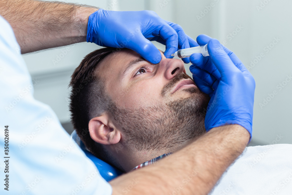 Handsome young man is getting a rejuvenating facial injections. He is sitting calmly at clinic. The expert beautician is filling male wrinkles by hyaluronic acid. Handsome young man is getting a rejuvenating facial injections. He is sitting calmly at clinic. The expert beautician is filling male wrinkles by hyaluronic acid.