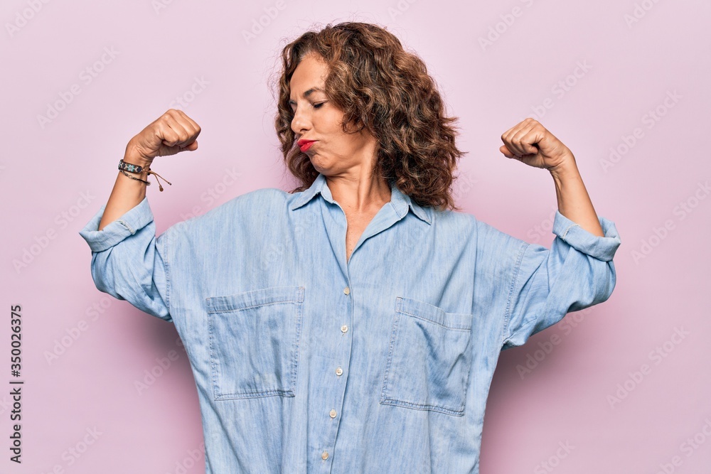 Middle age beautiful woman wearing casual denim shirt standing over pink background showing arms muscles smiling proud. Fitness concept. Middle age beautiful woman wearing casual denim shirt standing over pink background showing arms muscles smiling proud. Fitness concept.