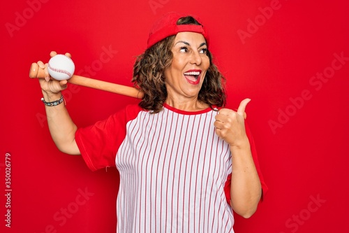 Photography Middle age senior woman wearing baseball equiment, bat and ball over red isolate