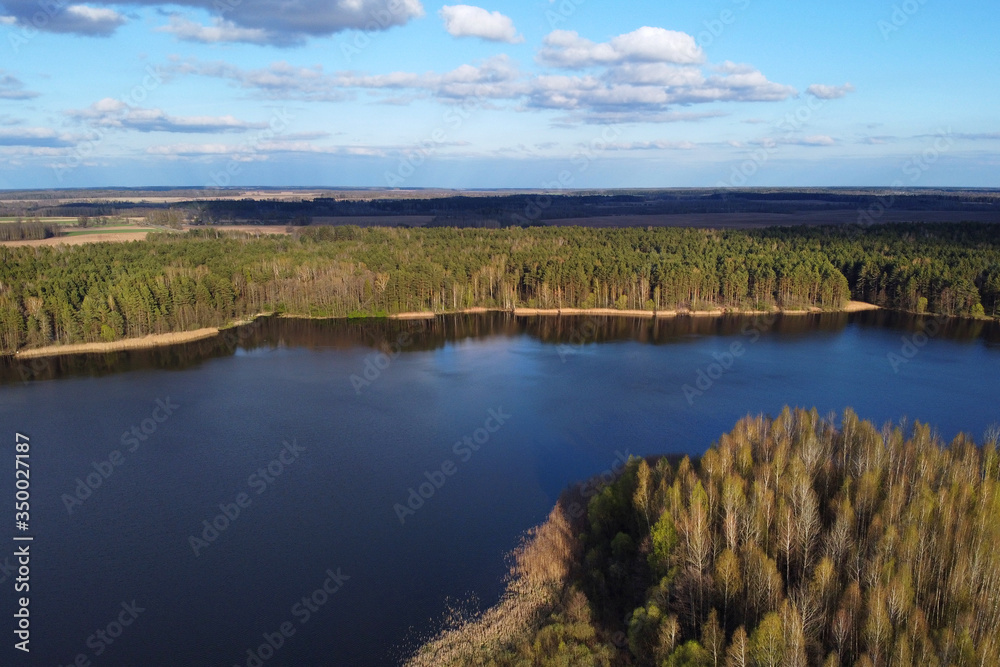 Forest lake, aerial shot of storage reservoir. Spring landscape with blue sky and white clouds at sunny day, river, European nature, top view. Forest lake, aerial shot of storage reservoir. Spring landscape with blue sky and white clouds at sunny day, river, European nature, top view.