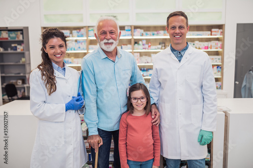 Professional pharmacists posing with customers in modern drugstore.