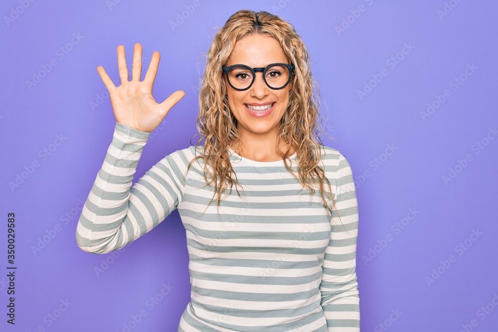 Beautiful blonde woman wearing casual striped t-shirt and glasses over purple background showing and pointing up with fingers number five while smiling confident and happy. Beautiful blonde woman wearing casual striped t-shirt and glasses over purple background showing and pointing up with fingers number five while smiling confident and happy.
