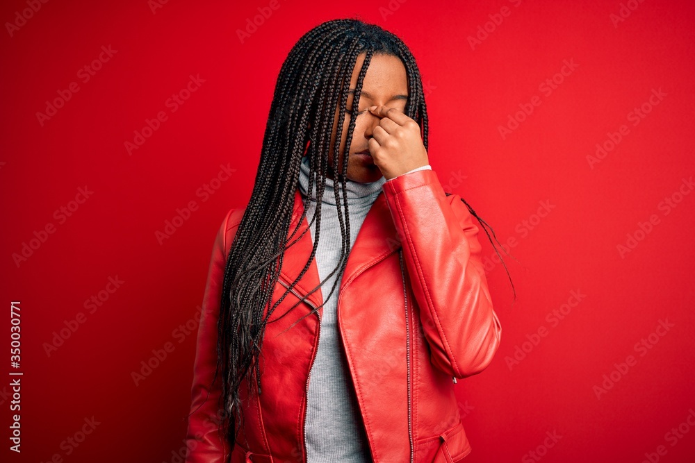 Young african american woman wearing cool fashion leather jacket over red isolated background tired rubbing nose and eyes feeling fatigue and headache. Stress and frustration concept.
