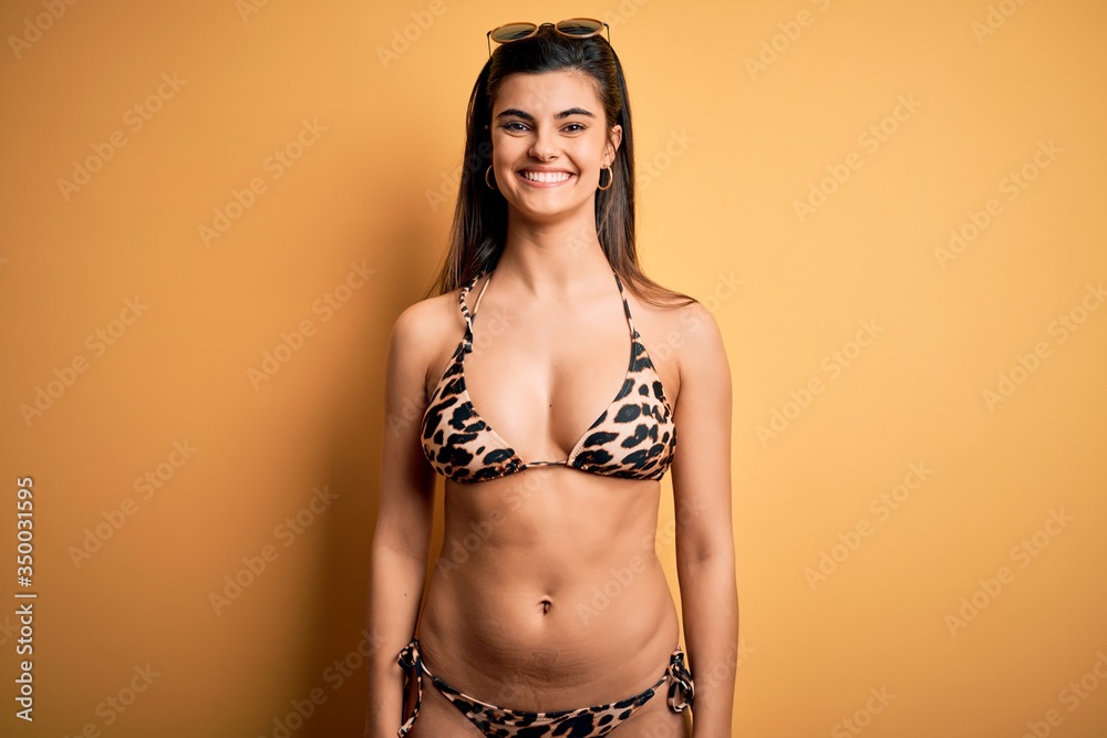 Φωτογραφία Young beautiful brunette woman on vacation wearing swimwear bikini over yellow background with a happy and cool smile on face