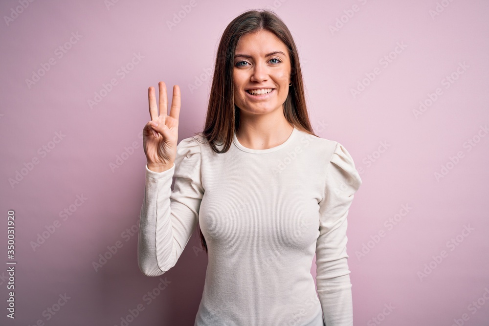 Young beautiful woman with blue eyes wearing casual white t-shirt over pink background showing and pointing up with fingers number three while smiling confident and happy. Young beautiful woman with blue eyes wearing casual white t-shirt over pink background showing and pointing up with fingers number three while smiling confident and happy.