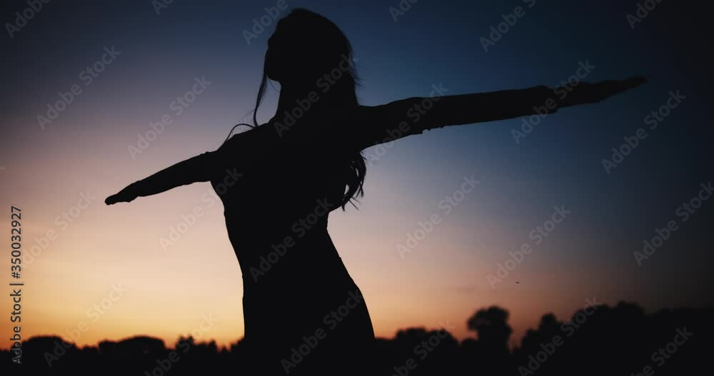 Young woman meditates at sunset in slow motion. Female silhouette on a background of the sun. Yoga practice outdoors in the evening Young woman meditates at sunset in slow motion. Female silhouette on a background of the sun. Yoga practice outdoors in the evening