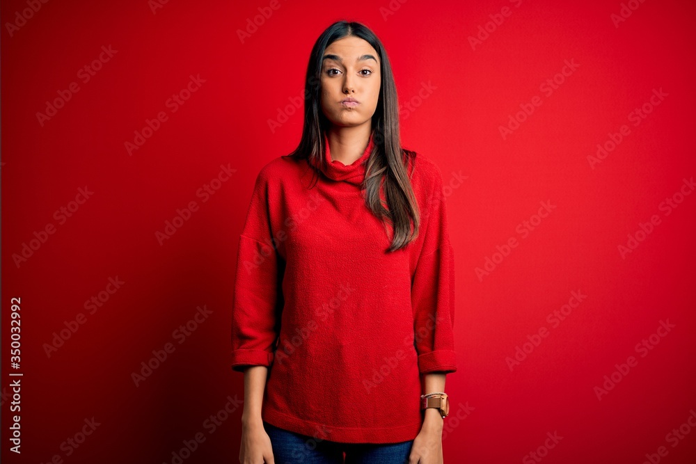 Young beautiful brunette woman wearing casual sweater over isolated red background puffing cheeks with funny face. Mouth inflated with air, crazy expression. Young beautiful brunette woman wearing casual sweater over isolated red background puffing cheeks with funny face. Mouth inflated with air, crazy expression.