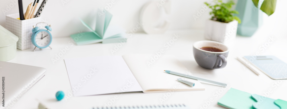 Fototapeta premium Creative desk with a blank picture frame or poster, desk objects, office supplies, books, and plant on a dark blue background.