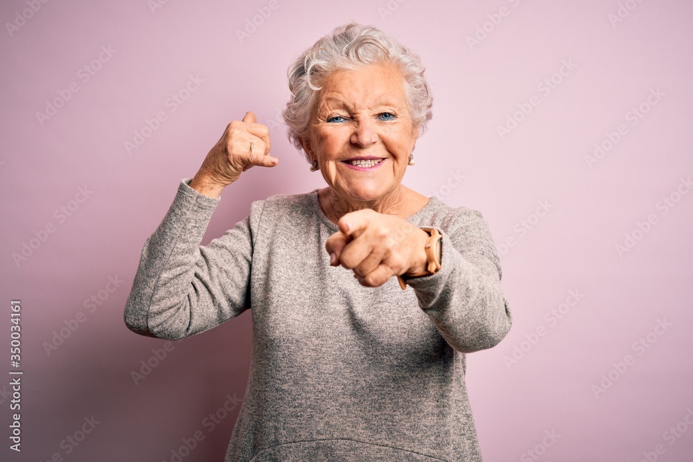 Senior beautiful woman wearing casual t-shirt standing over isolated pink background smiling doing talking on the telephone gesture and pointing to you. Call me. Senior beautiful woman wearing casual t-shirt standing over isolated pink background smiling doing talking on the telephone gesture and pointing to you. Call me.