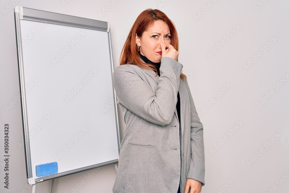 Φωτογραφία Young beautiful redhead businesswoman doing business presentation using magnetic board smelling something stinky and disgusting, intolerable smell, holding breath with fingers on nose