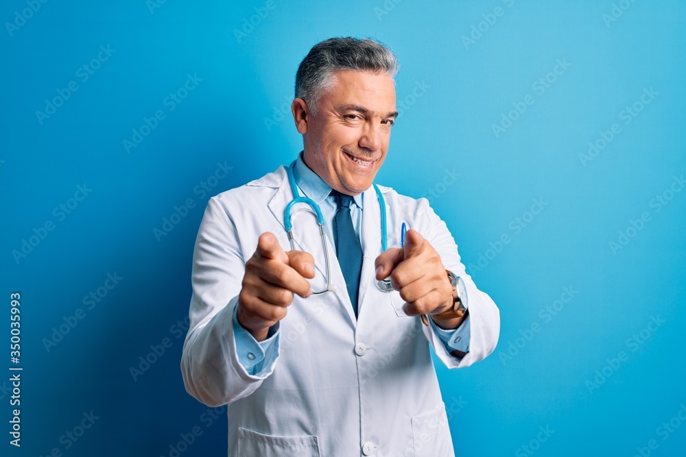 Middle age handsome grey-haired doctor man wearing coat and blue stethoscope pointing fingers to camera with happy and funny face. Good energy and vibes. Middle age handsome grey-haired doctor man wearing coat and blue stethoscope pointing fingers to camera with happy and funny face. Good energy and vibes.