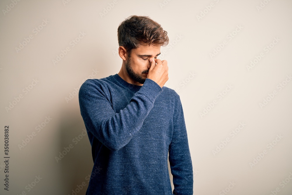Young handsome man with beard wearing casual sweater standing over white background tired rubbing nose and eyes feeling fatigue and headache. Stress and frustration concept. Young handsome man with beard wearing casual sweater standing over white background tired rubbing nose and eyes feeling fatigue and headache. Stress and frustration concept.