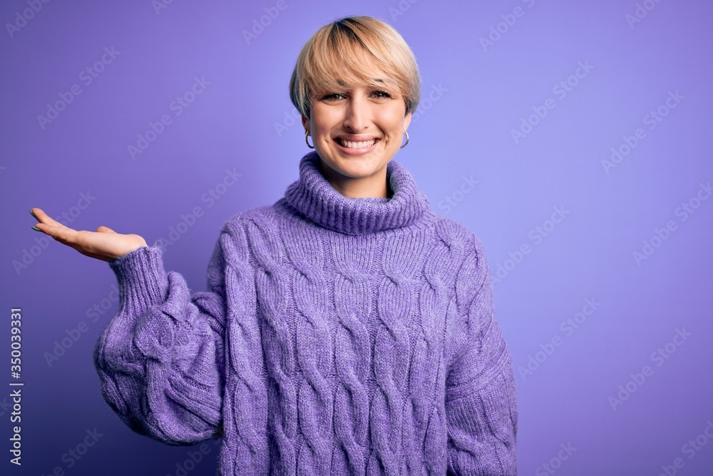 Young blonde woman with short hair wearing winter turtleneck sweater over purple background smiling cheerful presenting and pointing with palm of hand looking at the camera. Young blonde woman with short hair wearing winter turtleneck sweater over purple background smiling cheerful presenting and pointing with palm of hand looking at the camera.