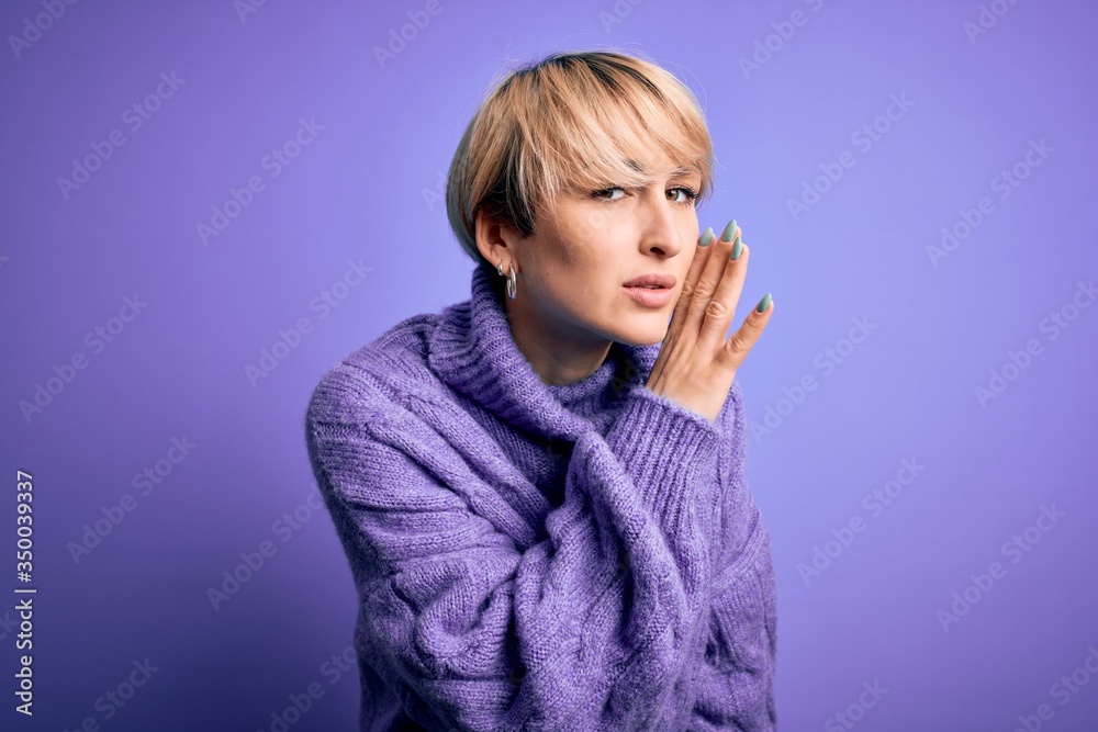 Young blonde woman with short hair wearing winter turtleneck sweater over purple background hand on mouth telling secret rumor, whispering malicious talk conversation Young blonde woman with short hair wearing winter turtleneck sweater over purple background hand on mouth telling secret rumor, whispering malicious talk conversation