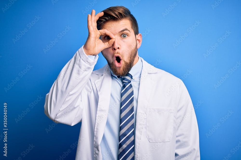 Young blond therapist man with beard and blue eyes wearing coat and tie over background doing ok gesture shocked with surprised face, eye looking through fingers. Unbelieving expression. Young blond therapist man with beard and blue eyes wearing coat and tie over background doing ok gesture shocked with surprised face, eye looking through fingers. Unbelieving expression.