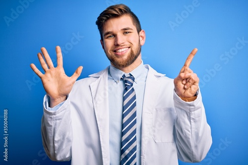 Young blond therapist man with beard and blue eyes wearing coat and tie over background showing and pointing up with fingers number six while smiling confident and happy.