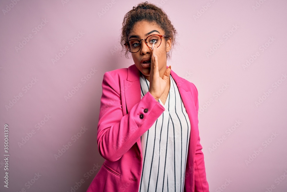 Beautiful african american businesswoman wearing jacket and glasses over pink background hand on mouth telling secret rumor, whispering malicious talk conversation Beautiful african american businesswoman wearing jacket and glasses over pink background hand on mouth telling secret rumor, whispering malicious talk conversation