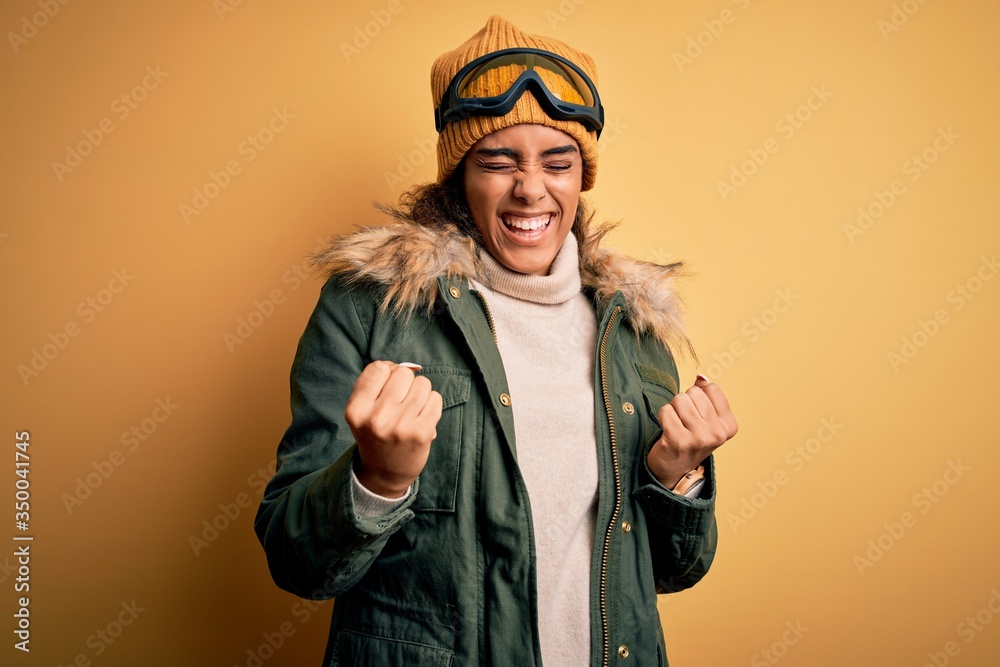 Young african american afro skier girl wearing snow sportswear and ski goggles celebrating surprised and amazed for success with arms raised and eyes closed. Winner concept.